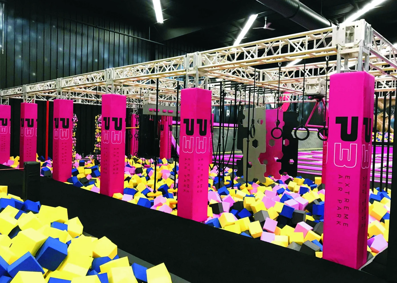 Indoor adventure play area with suspended padded obstacles and a foam landing pit
